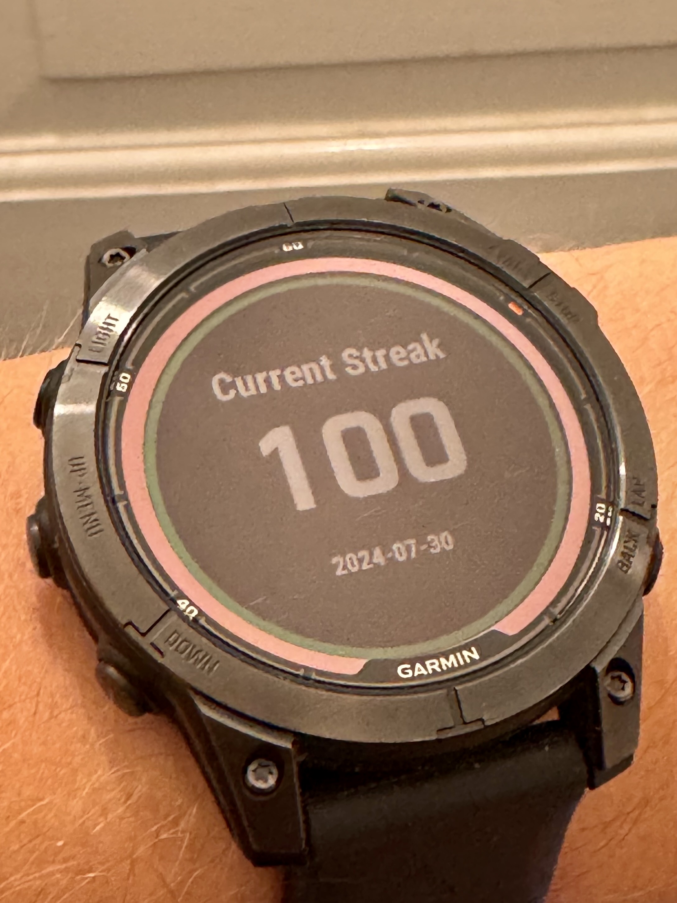A black Garmin watch displaying the number 100, indicating a 100 day run streak